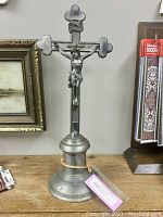 Full view of silver-toned altar crucifix showing full height and base on wooden surface with adjacent items