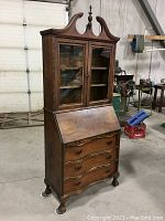 Overall front view of closed desk showing serpentine profile, glass doors, drop front and carved feet