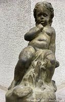 Front view of the concrete cherub statue showing the front sitting pose with hand near chin.