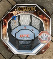 Front view of UFC Octagon play set box showing the cage and one UFC fighter figure attached to the cage.