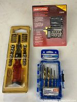 Overall view of the ratchet and screwdriver set in yellow packaging, Mastercraft drill and extractor bit set in blue plastic case, and Craftsman mini driver bit set in red packaging