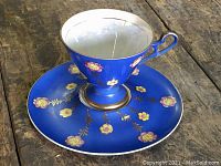 Photo showing full teacup and saucer set together on wooden surface with blue base and hand-painted yellow and pink flowers.