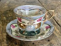 Teacup and saucer set displayed on a wooden surface showing sky blue color, gold accents, floral pattern, and unique three-footed base of the cup.