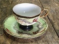 Teacup and saucer set on wooden surface showing dragon design and gold handle.