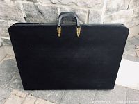 Full view of the large black hard leather portfolio case showing its rectangular shape and leather handle.
