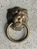 Front view of antique brass lion head furniture pull showing detailed lion face and attached ring.