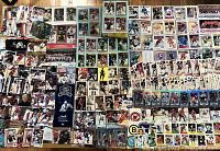 Photo showing a large assortment of hockey cards and some other sports cards arranged covering a surface including team and player cards from various years.