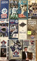 Top view of the lot showing 11 Toronto Blue Jays baseball media and official guides in good condition, some with player images such as Kelly Gruber and Eric Hinske, includes one with a small piece cut out from the cover.