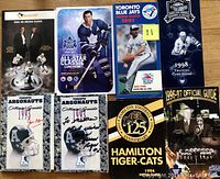 Multiple sports media guides including 1993 Toronto Argonauts signed guides, 1994 Hamilton Tiger-Cats guide, 1991 Toronto Blue Jays guide, NHL All-Star Classic program, and 1996-97 Toronto Maple Leafs official guide.