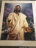 Full view of the framed print showing Jesus in a cream robe with his hands extended, surrounded by purple flowers and greenery.