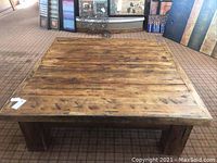 Large square wood coffee/all-purpose table with rustic finish and thick legs. Top is made from multiple wooden planks with visible grain and wear.