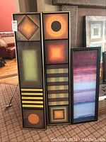 Three vertical abstract art panels in various geometric and color block designs including squares, circles, and stripes.