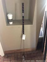 Full view of 45 inch Adams Golf graphite shaft chest putter standing upright next to a coffee cup on a shelf for scale.