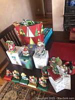 Photo showing 9 Christmas stocking hangers figurines on green and gold bases along with gift bags and other decor on a table