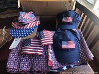 Photo showing multiple American flag themed hats, caps, and scarves stacked on a table.