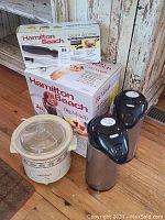 Lot of kitchenware showing Rival small crockpot with floral pattern, Hamilton Beach juicer and electric knife boxes, and two Thermos stainless steel coffee pots.