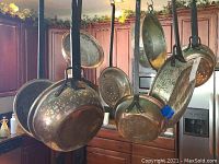 Multiple copper pots and pans hanging by wrought iron handles
