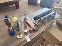 Ten pieces displayed on a wooden surface: candle holders of various materials including metal, glass, and wood; several candles; and a rectangular metal light sconce with wiring.