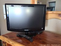 Samsung 18 inch TV on stand with remote in front displayed on wooden surface.