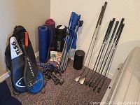 Wide view showing all exercise and sports equipment including yoga mats, golf clubs, tennis rackets, hand weights, foam roller, and chair.