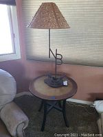 Full view of the round coppertop side table with black metal legs and a decorative lamp on top (lamp not included).