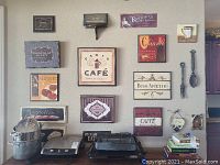 Wide view of all 18 wooden wall decor plaques and small shelf arranged on a beige wall above cabinetry. Mostly café and food themed with various sizes and colors. Includes metal cutlery decor and hanging plaques.