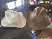 Two men's western felt hats, light-colored and brown, placed on a counter to show full hats