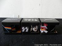 Three boxed ceramic rock band mugs from Pink Floyd, Kiss, and Metallica set side by side showing band logos on boxes.