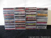 Stacks of assorted music CD cases showing album covers and spines, arranged in rows against a plain wall.