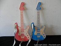 Both red and blue wooden toy guitars shown together against white wall and black surface.