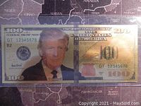 Front side of the $100 note featuring a portrait of Donald Trump with gold accents and serial number DT 12345678.