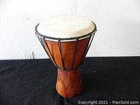Front perspective of the djembe hand drum showing the natural drumhead and wooden body with black ropes for tuning.