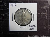 Obverse side of 1942 Walking Liberty half dollar coin in protective holder showing Lady Liberty walking with sun and branches, signed silver 9000 on holder.