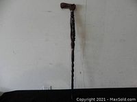 Full length view of the wooden carved walking cane standing upright showing its length and design.