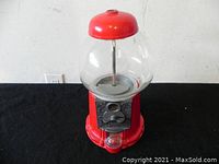 Front angled view of gum machine showing red metal base and top, clear glass globe, and coin mechanism.