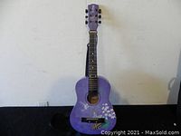 Full front view of the purple Disney by Washburn acoustic guitar with Hannah Montana design showing the body, fretboard, and headstock.