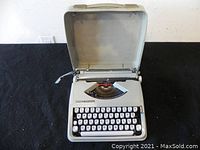 Open view of the Hermes Baby typewriter placed inside its hinged carrying case on a black fabric surface.