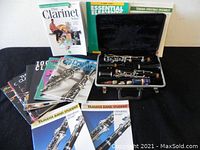 Vintage Bundy clarinet in black velvet-lined case, with all component parts disassembled and placed inside. Surrounding the case are multiple clarinet instructional and sheet music books.