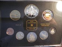 Top down view of the eight-coin proof set displayed in black holder, showing the silver dollar, gold plated twoonie and other denominations with Royal Canadian Mint logo in the center.