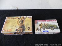 Shows two boxed model kits on a black surface, highlighting the Da Vinci mechanical model and Russian Field Car GAZ67B model kits side by side.