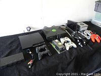 Full overview of the lot on black cloth including Xbox, Nintendo GameCube, Wii, Nintendo 64 consoles, controllers and cables.