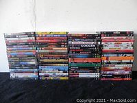 Stack of assorted DVD movies arranged in four vertical piles against a white wall on black surface.