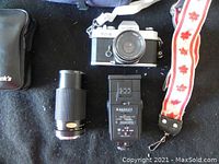 Photo of Yashica FX-2 camera with Yashica 50mm lens, telephoto lens, flash, and camera strap arranged on a black surface