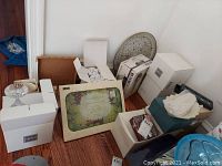 Multiple boxed and unboxed kitchenware items including stemware, trays, and trivet on wooden floor.