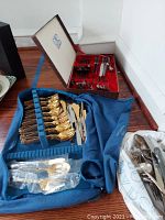 Overview of flatware sets and loose pieces on floor, showing red box, blue roll, and plastic bag with flatware