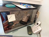 Oster microwave front view showing reflective black glass door with a note indicating microwave dimensions (20x15x12 inches).