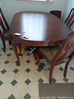 Full view of dining table with curved legs and attached chairs, showing overall shape and surface wear.