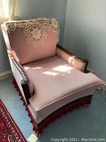 Full view of vintage single chair with pink fabric and crochet doily on backrest, situated on carpeted floor near window with sunlight.