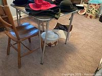 Photo showing vintage metal folding card table with items on top and wooden chair beside it on carpeted floor.