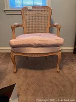 Front view showing cane backrest, pink cushioned seat, and carved wooden legs and arms.